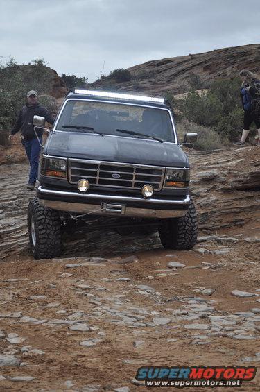 1991 Ford Bronco with large tires and light bar driving on a rocky trail