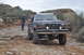 1991 Ford Bronco - A lifted Ford F-Series truck navigates a challenging, rocky terrain with a person observing the path ahead.