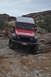 1991 Ford Bronco - A red Jeep Wrangler navigates a challenging rocky terrain under an overcast sky.