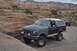 1991 Ford Bronco - Two off-road vehicles, a Ford Bronco and a Jeep Wrangler, navigate a rocky trail in a desert landscape.