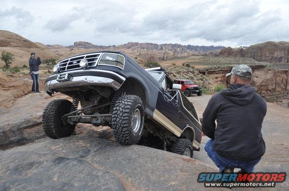 Dark blue Ford Bronco with gold trim on rocky terrain, front right wheel elevated