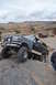 1991 Ford Bronco - A dark blue Ford Bronco with a tan stripe navigates rocky terrain, with a red Jeep in the background.