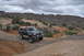 1991 Ford Bronco - A dark blue Ford Bronco navigates a rocky off-road trail under a cloudy sky.