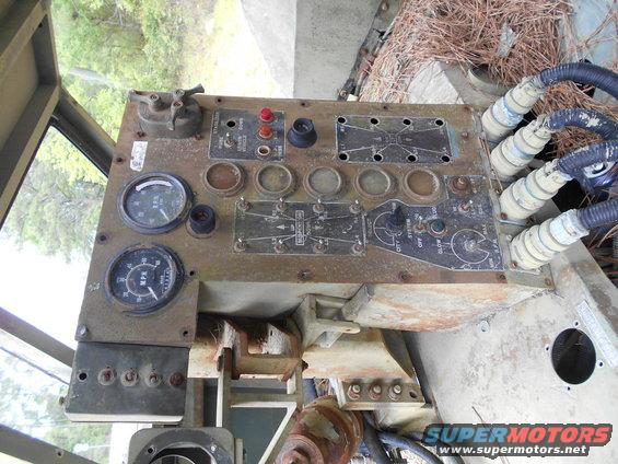 Close-up of a rusty vehicle dashboard with two gauges, multiple switches, and electrical connectors