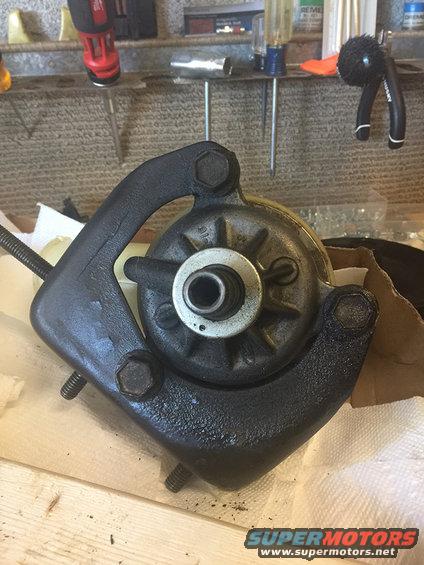 Black metal automotive part with bolts and a central shaft, resting on paper towels