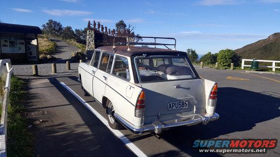 old white station wagon with roof rack parked, luggage inside, at a scenic overlook with a monument and information sign