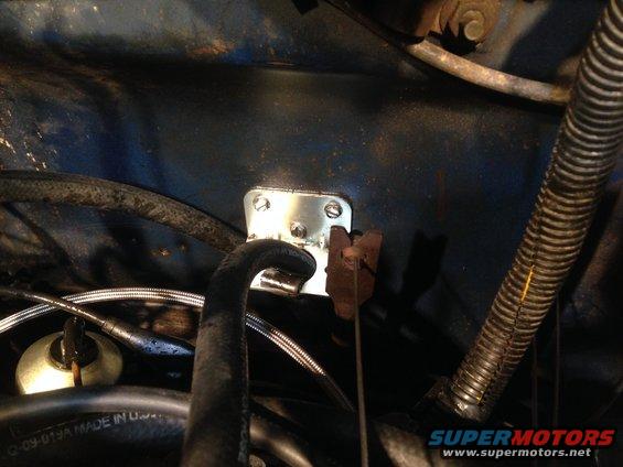 Metal bracket with screws attached to blue painted surface, near hoses and wiring