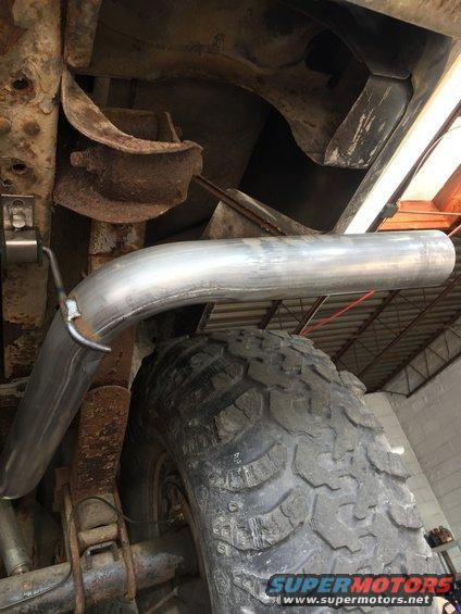 Exhaust pipe curving over a large, knobby tire on a rusty vehicle chassis