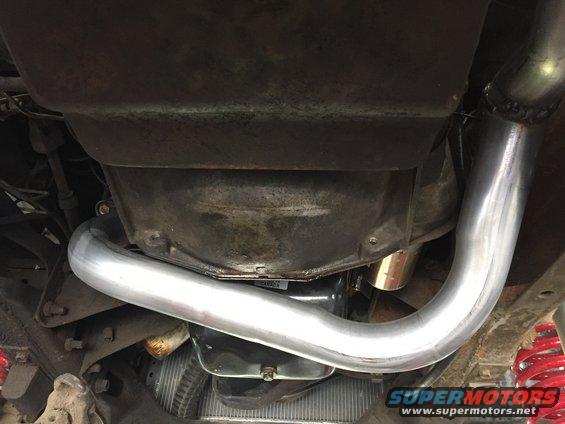 Underneath view of a vehicle's transmission housing and a shiny new exhaust pipe. Red coil springs are visible