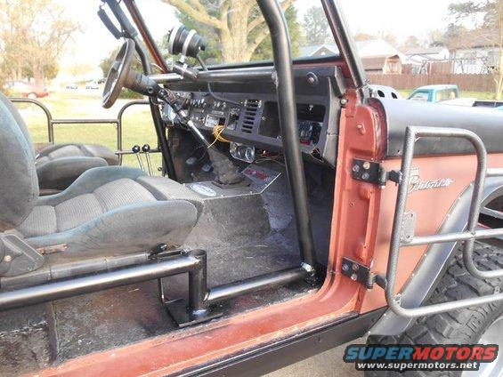 Interior of a modified Ford Bronco with roll cage, bucket seats, and custom door panel