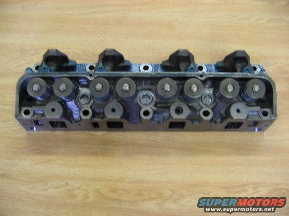 Engine cylinder head with visible valves and springs on a wooden surface