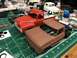 1989 Ford Bronco - Two model trucks, a red 1956 Ford F-100 and a brown one, sit on a green cutting mat surrounded by model building supplies.