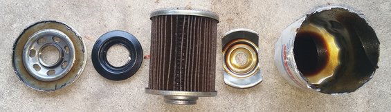 Disassembled oil filter with metal canister, filter element, gasket, and end cap on concrete