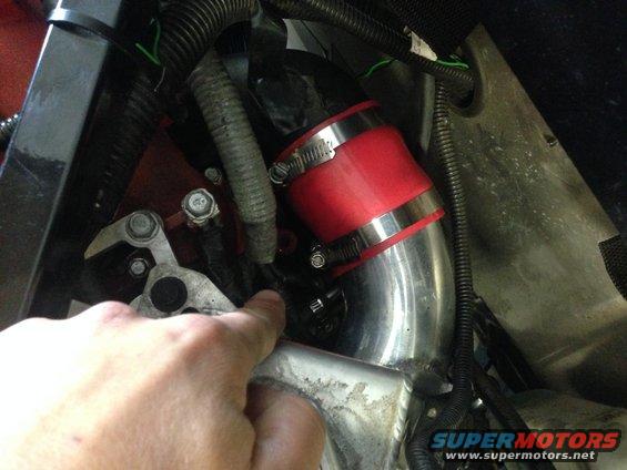 Close-up of a red silicone coupler on a metal intake pipe in an engine bay