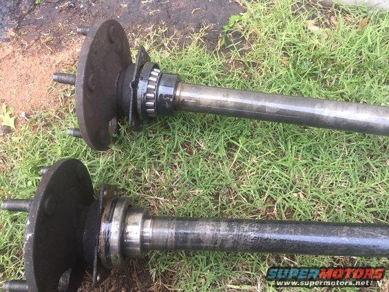 Two vehicle axle shafts with hubs and bearings are lying on the grass