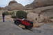 1991 Ford Bronco - A red Jeep Wrangler navigates a steep, rocky trail in a desert landscape with onlookers.