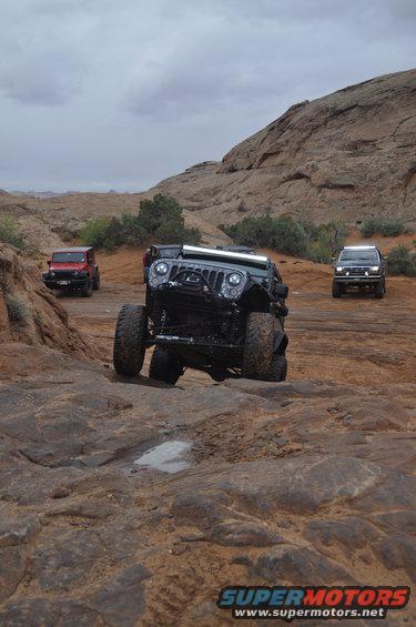 Three Jeeps driving on a rocky desert trail under a cloudy sky