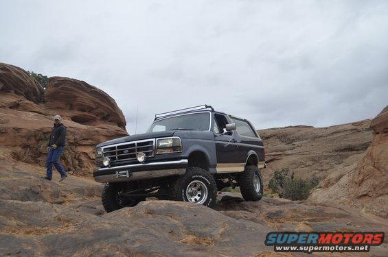 1991 Ford Bronco on rocky terrain, front 3/4 view, dark blue with tan trim