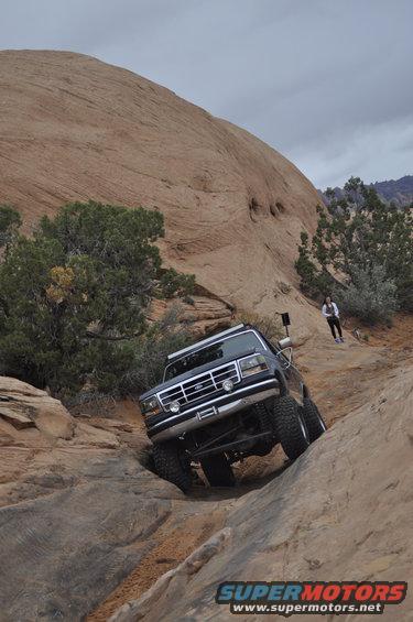 Ford F-series truck climbing a rocky trail, person watches from above