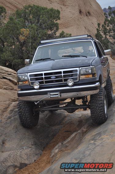 Dark gray Ford Bronco with off-road tires and a light bar on top, driving over rocks