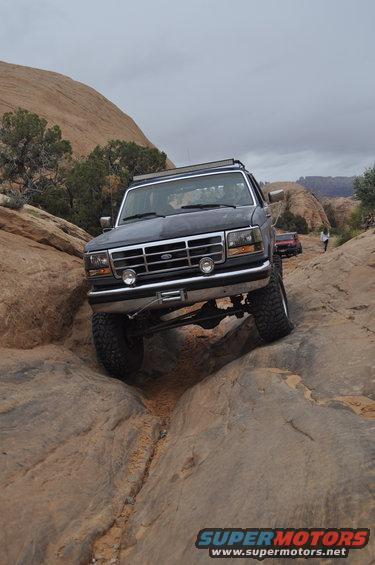 Dark 1991 Ford Bronco climbing rocks on off-road trail