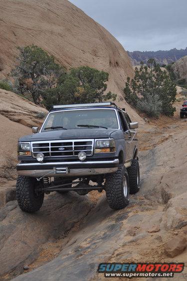 Dark blue Ford Bronco off-roading on a rocky trail, front winch, light bar