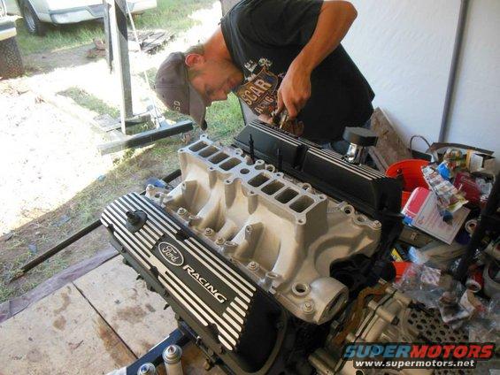 Ford Racing valve cover and intake manifold on engine stand, man working on it