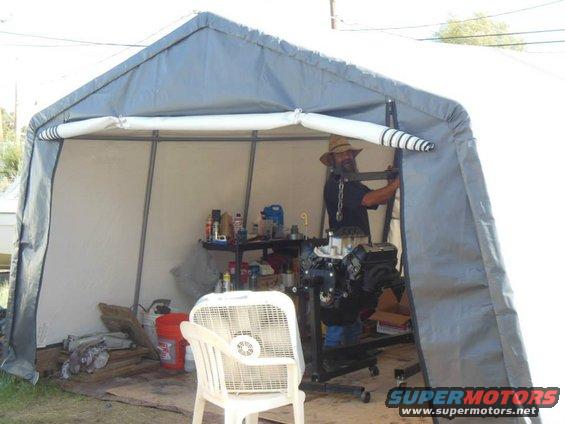 Engine on stand inside a portable garage, with a man working on it