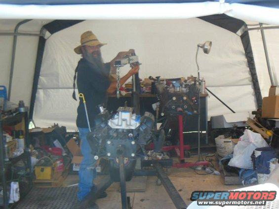 Man in straw hat works on engine in garage. Another engine is on a stand nearby