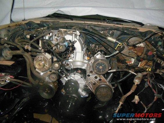 Engine bay with various hoses, belts, and components visible. Some parts are covered by a white tarp