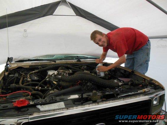 Man in red shirt pouring fluid into engine bay of a truck