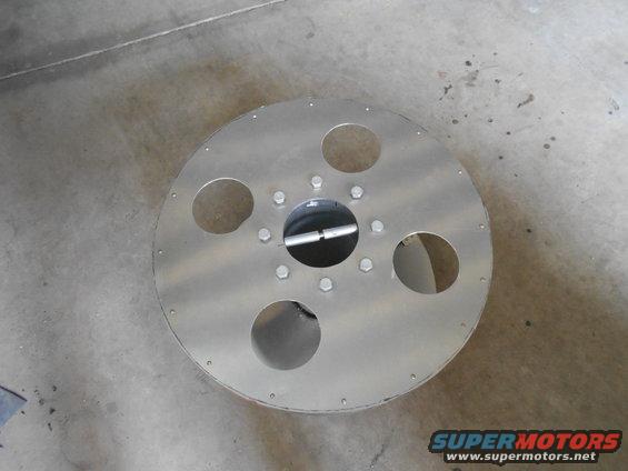 Aluminum wheel with five circular cutouts and a central hub, bolted to a concrete floor