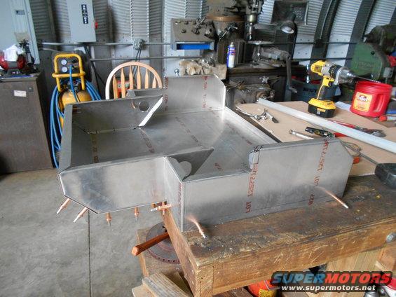 Unfinished aluminum fabrication project on a workbench with tools and machinery in the background