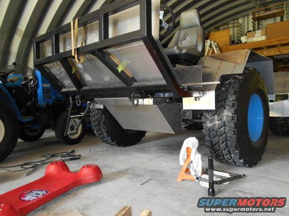 Custom vehicle with large tires and cargo bed, blue tractor in background