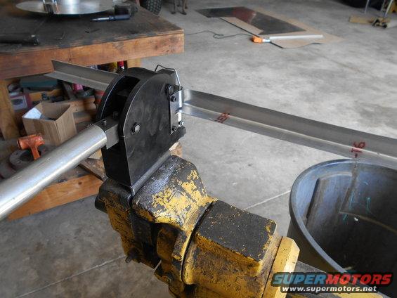 metal stock being bent in a yellow vise with a black tool