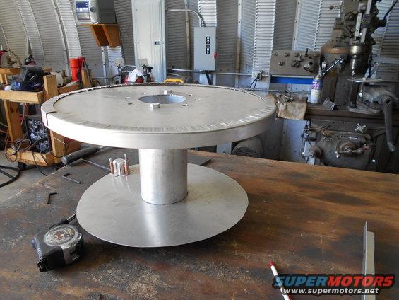Large metal spool on workbench with tape measure and pencil