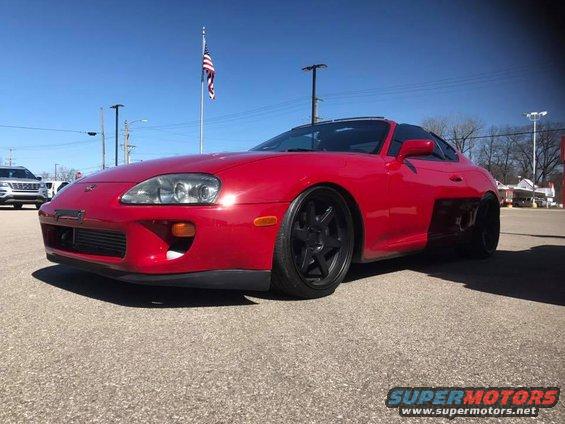 Red Toyota Supra with black aftermarket wheels, front 3/4 view, lowered suspension
