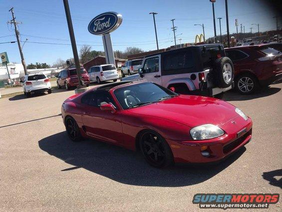 Red 1994 Toyota Supra parked in lot with other vehicles and a Ford sign