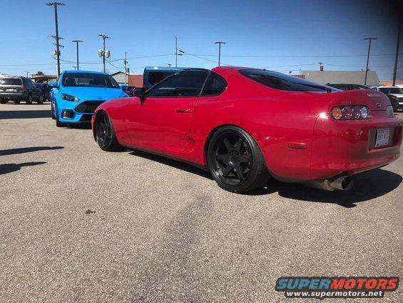 Red sports coupe parked next to a blue hatchback. Rear view shows black wheels and a spoiler