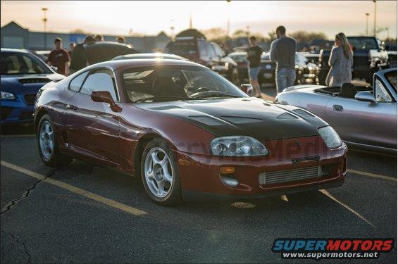 Red 1994 Toyota Supra with black hood parked in lot, other cars around