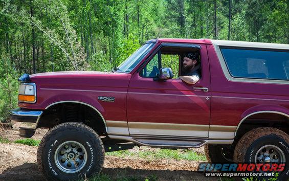 Side view of a red 1995 Ford Bronco with a man driving