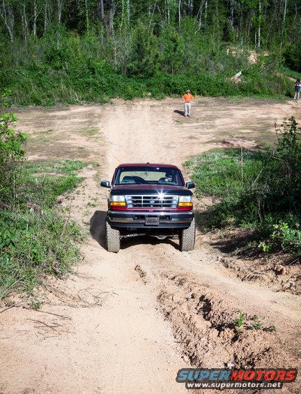 Red 1995 Ford Bronco driving on a dirt road