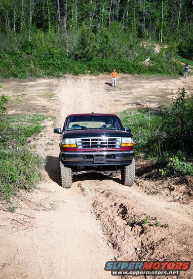 1995 Ford Bronco driving up a dirt hill with two people in the background