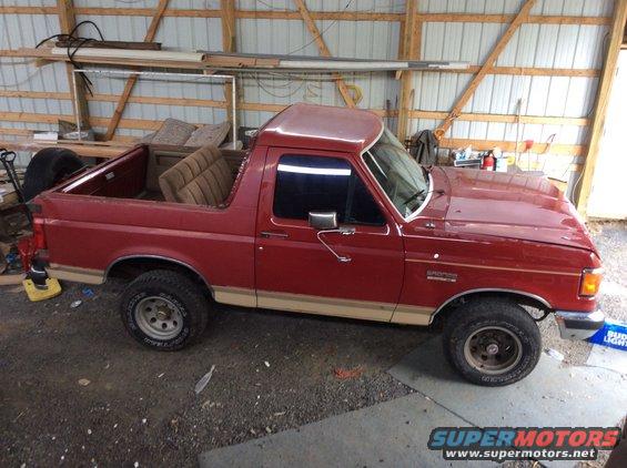 Red 1989 Ford Bronco parked inside a garage with tan interior seats visible in the bed