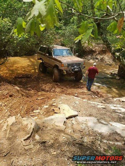 Brown Ford Bronco with off-road modifications navigating a muddy stream