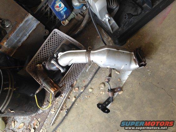 Catalytic converter removed from a vehicle, lying on a concrete floor next to some tools and a plastic crate