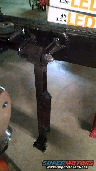 Close-up of a black metal suspension part attached to a vehicle frame. Boxes labeled 'LED' are in the background