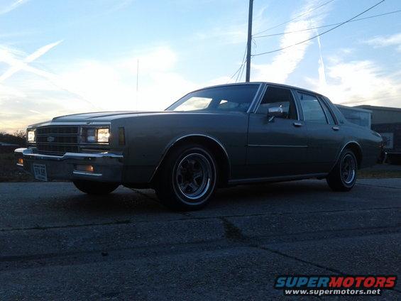 Gray 1980s Chevrolet Caprice sedan parked on asphalt, front 3/4 view, cloudy sky
