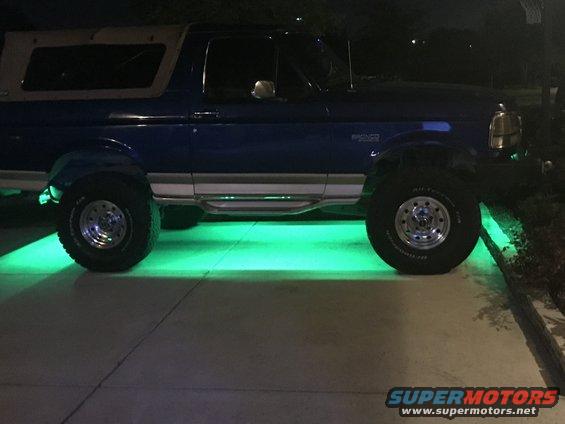 Blue Ford Bronco with tan top, side view, green underglow lights