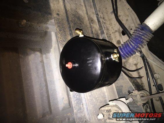 Black air tank with brass fittings and a red cap, mounted under a vehicle